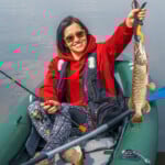 Kayak fishing. Fisher girl holding pike fish trophy